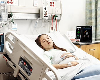 Paciente en la cama del hospital usando un sensor Masimo con un dispositivo Root al fondo.