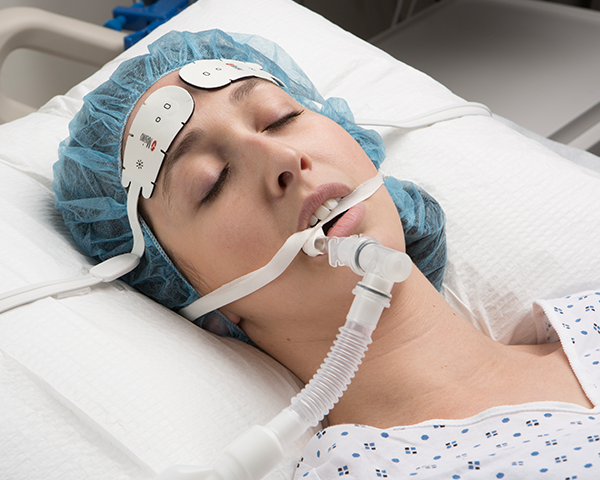 Paciente dormido intubado con bata de hospital y gorro quirúrgico monitorizado mediante un sensor frontal Masimo