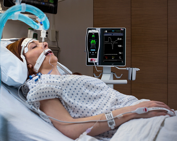 Paciente dormido intubado en una cama de hospital monitorizado mediante un sensor de dedo con monitorización Root y Radical-7 junto a la cama.