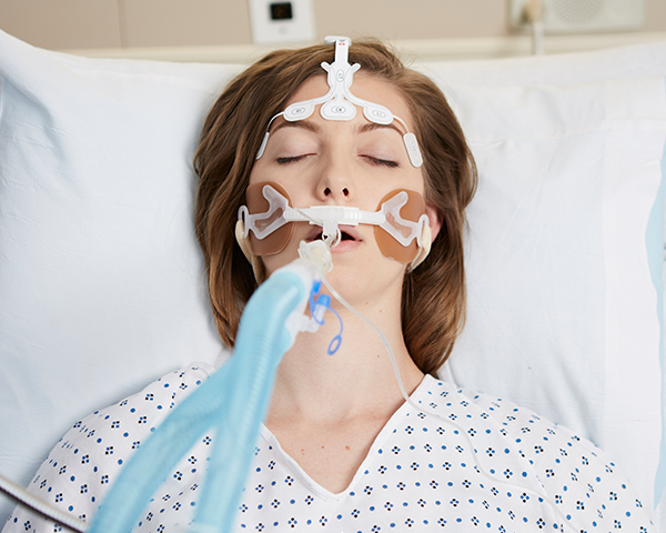 Paciente dormido intubado con bata de hospital monitorizado mediante un sensor frontal Masimo
