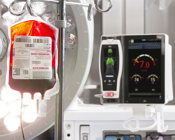Bolsa de sangre para transfusión intravenosa colgada junto a un dispositivo para monitorización de cabecera.