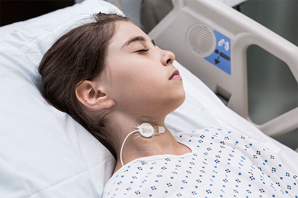 Masimo - Niño con el sensor RRa de frecuencia respiratoria acústica en el cuello mientras está en la cama del hospital